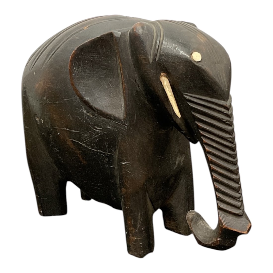 African Elephant Ebonized Wood Carving with Inlays: An appealing hand-carved ebonized wooden sculpture depicting a stylized standing elephant. The figure showcases a deeply ridged, downward-curving trunk resting near the feet, stylized flared ears, and