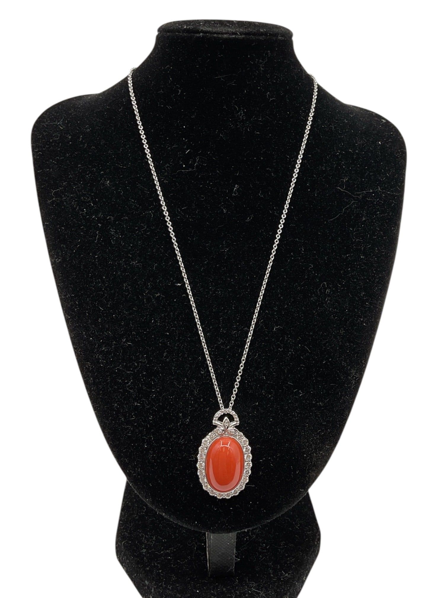 Coral and Diamond Pendant Necklace: An elegant pendant necklace featuring an oval cabochon coral centerpiece surrounded by a halo of sparkling natural diamonds. The pendant is topped with a decorative diamond-set bow motif and suspended