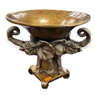 Decorative Elephant Form Pedestal Bowl with Dual Head Base: This impressive decorative pedestal bowl features a wide shallow basin supported by a sculptural base formed by two opposing elephant heads with raised trunks. Finished in warm bronze tones, the piece