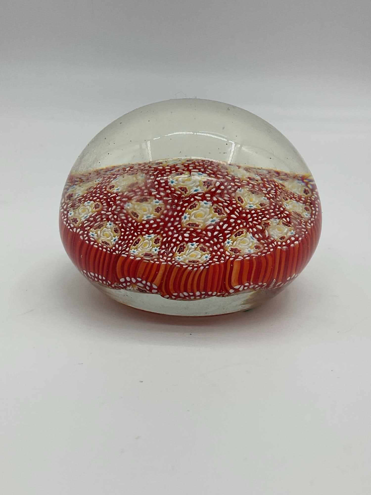 Millefiori Glass Paperweight with Red and Yellow Floral Canes: Decorative glass paperweight featuring intricate millefiori cane work in red, yellow, white, and blue patterns, forming symmetrical floral designs under a clear glass dome. Dimensions: H3in Diameter 4