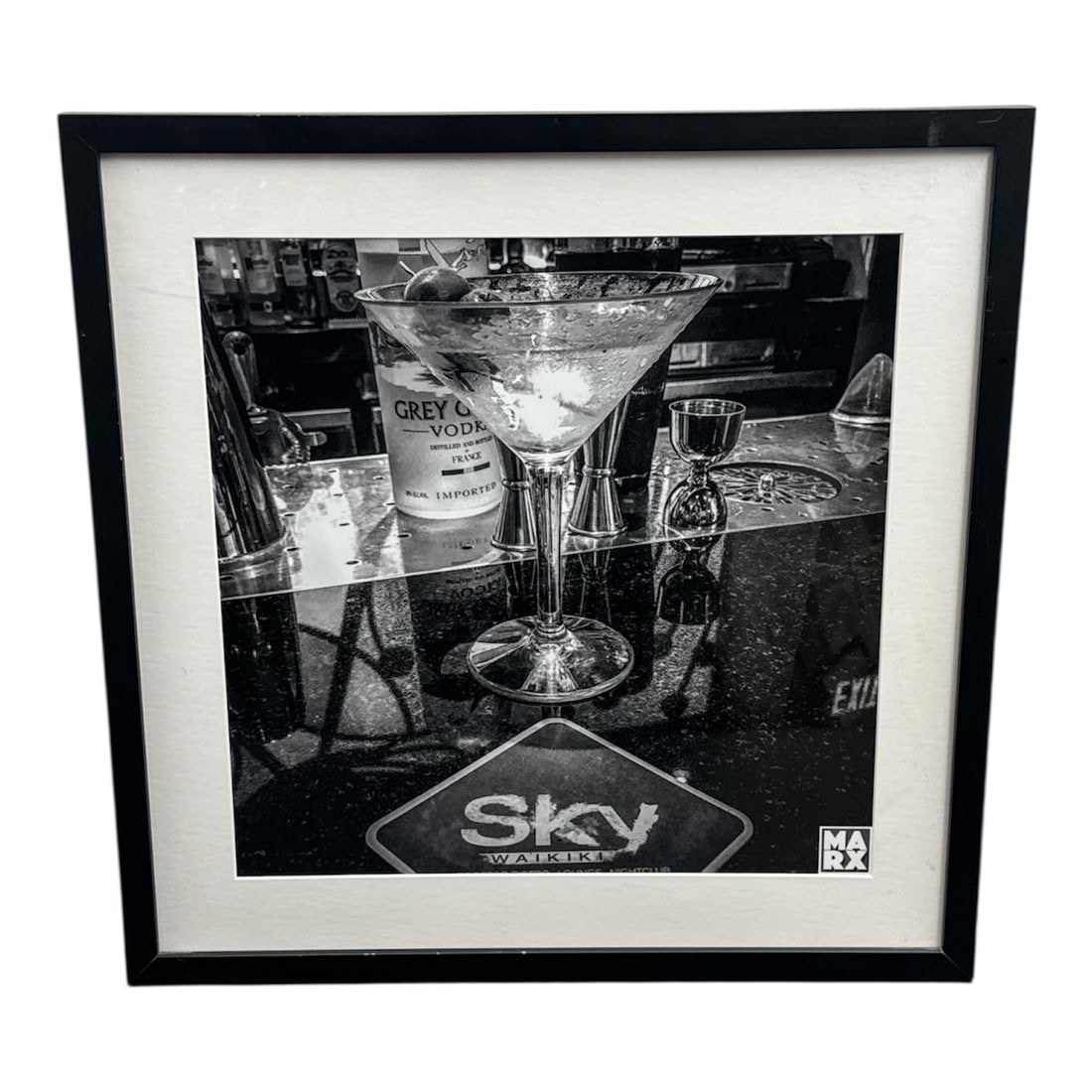 Black and White Photographic Print of Martini Still Life by MARX, Framed: This black and white photographic print depicts a stylized martini still life, featuring a cocktail glass set against a bar scene with liquor bottles and reflective surfaces. The composition emphasize