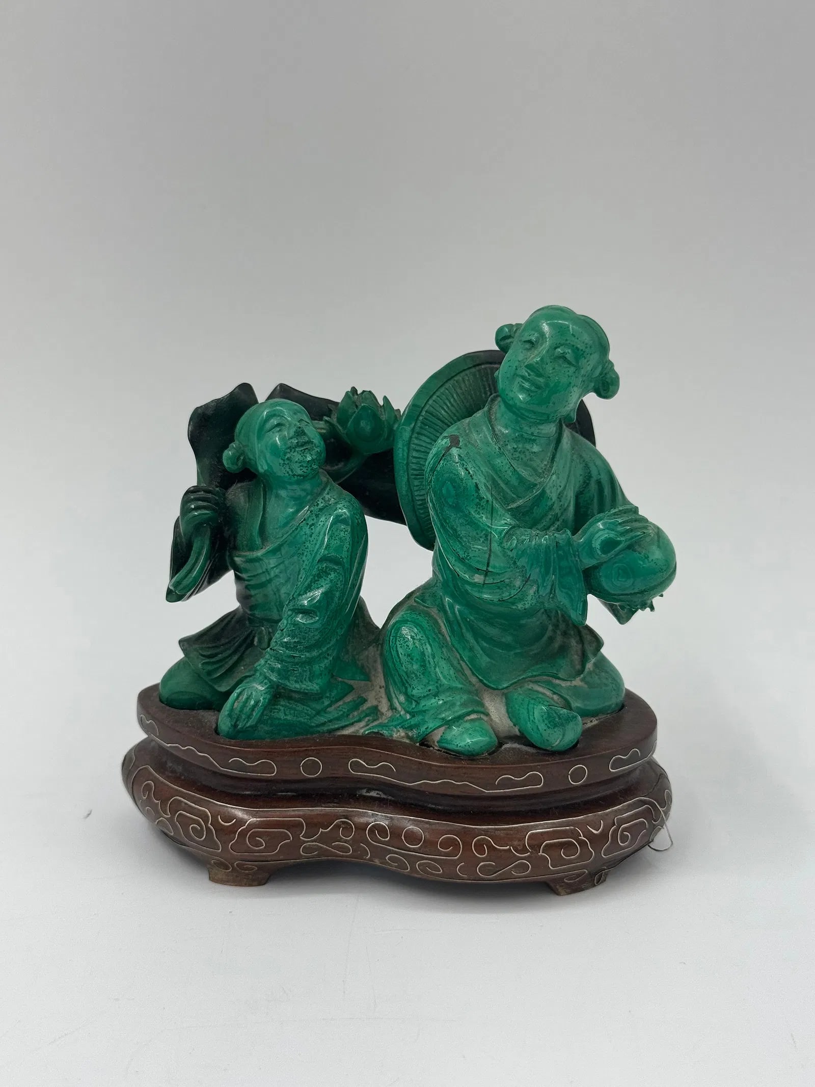 Chinese Carved Malachite Figure on Stand: A carved malachite figure depicting a man with a hat and a circular object, mounted on a decorative wooden stand. Dimensions: 4.5 x 4.5 x 2 inches. 
