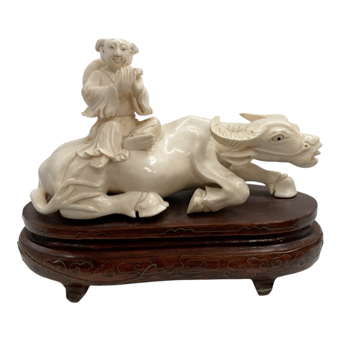 Asian-Style Carved Water Buffalo with Child Figural Sculpture: A detailed Asian-style carved sculpture depicting a reclining water buffalo with a young child seated upon its back. The child is shown in traditional attire, while the buffalo features expressive fac