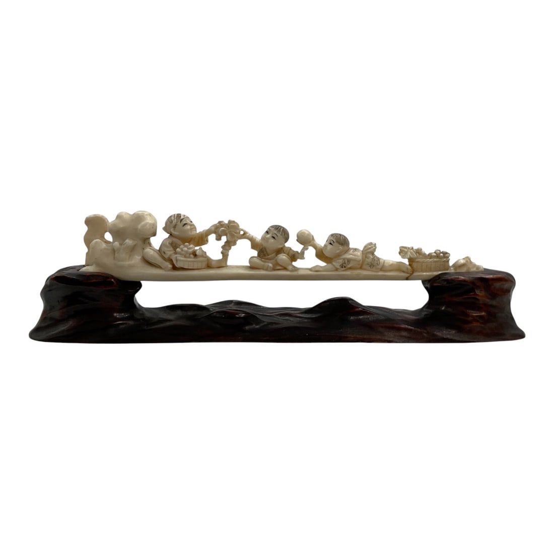 Asian-Style Carved Children Figural Sculpture on Wood Stand: A decorative Asian-style carved sculpture depicting a procession of playful children arranged along an elongated composition. The figures are shown in varied poses interacting with one another and car