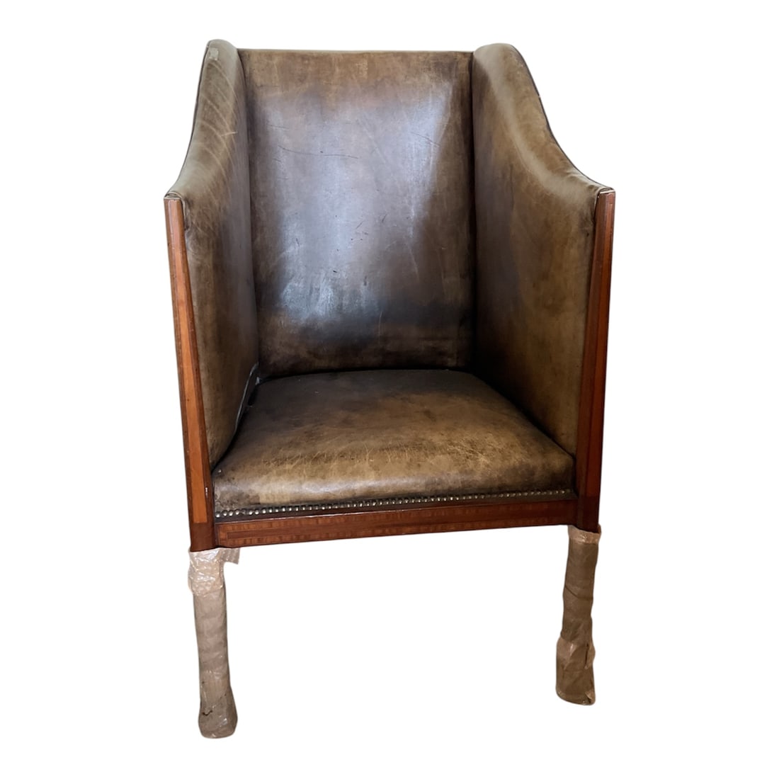 Neoclassical Style Leather Upholstered Barrel Armchair: A Neoclassical style barrel-back armchair upholstered in patinated distressed brown leather. Features high sloping sides and a squared tight seat outlined with brass nailhead trim. The exposed mahogan