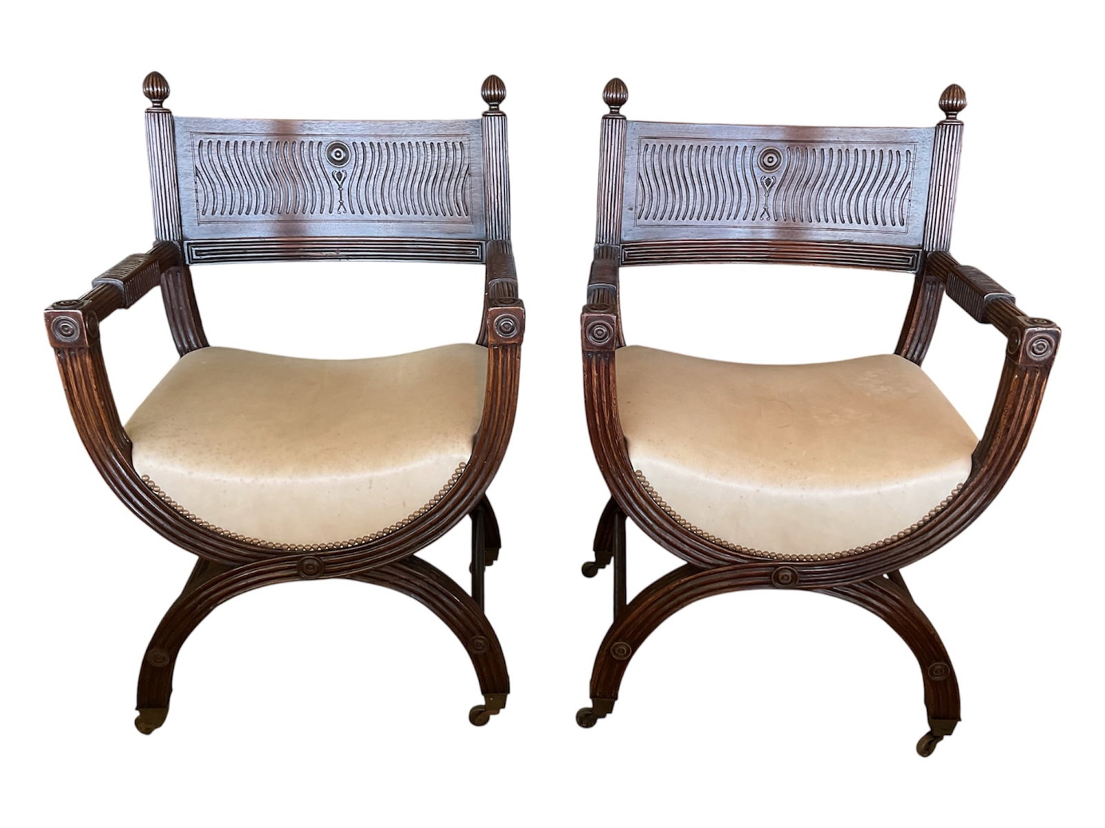 Pair of Regency Style Carved Mahogany Curule Armchairs: A pair of Regency style carved mahogany curule-form armchairs. Each features a curved back splat detailed with fluted channels and carved rosettes, topped with finial posts. The open curved armrests l