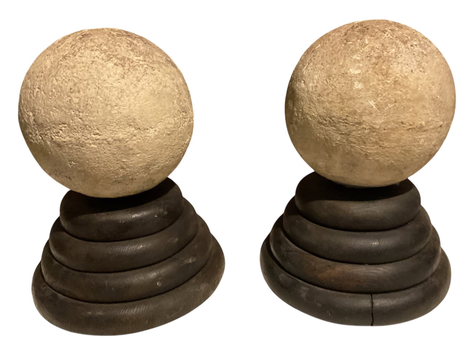 Pair of Textured Stone Spheres on Tiered Wooden Stands: Pair of decorative objects featuring roughly textured spherical forms in a warm beige stone-like material, each presented on a dark turned wooden stand. The stands are constructed with graduated circu