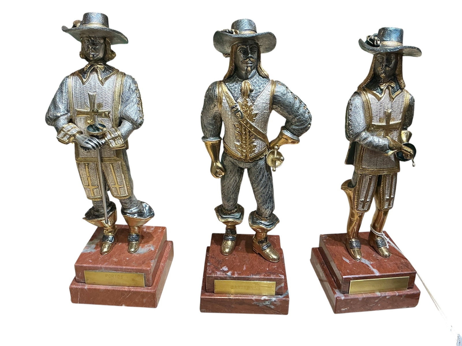 BR266- Set of Three Musketeer Figures in Bronze with Gold Finish on Marble Bases: A decorative set of three musketeer figures crafted in bronze with a gold-toned finish, each mounted on a polished marble base. The figures are depicted in classic period attire, including wide-brimme