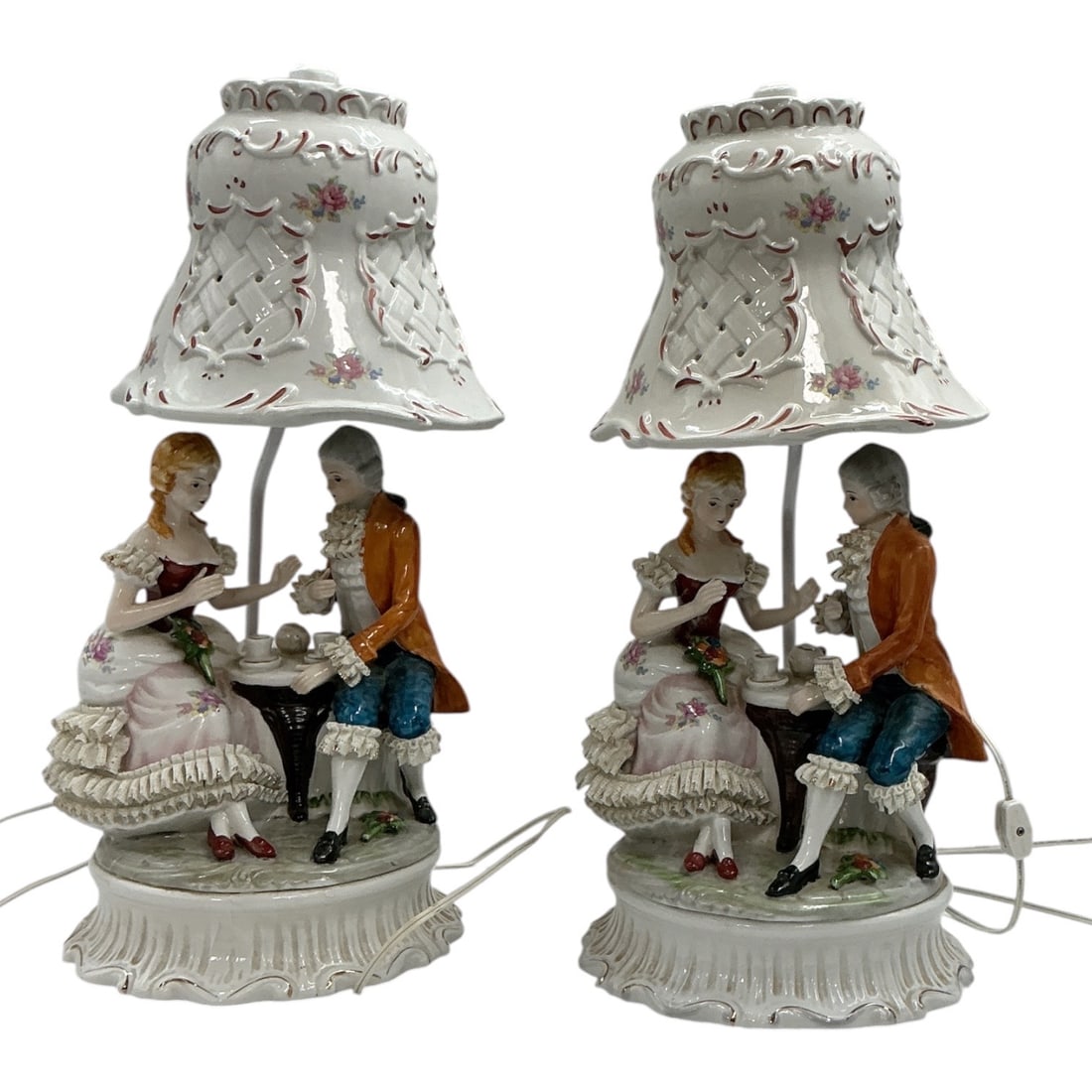 Pair of Capodimonte Style Porcelain Figural Table Lamps: Decorative pair of Capodimonte-style porcelain figural table lamps, each depicting an elegantly dressed courting couple seated at a tea table beneath an ornate pierced