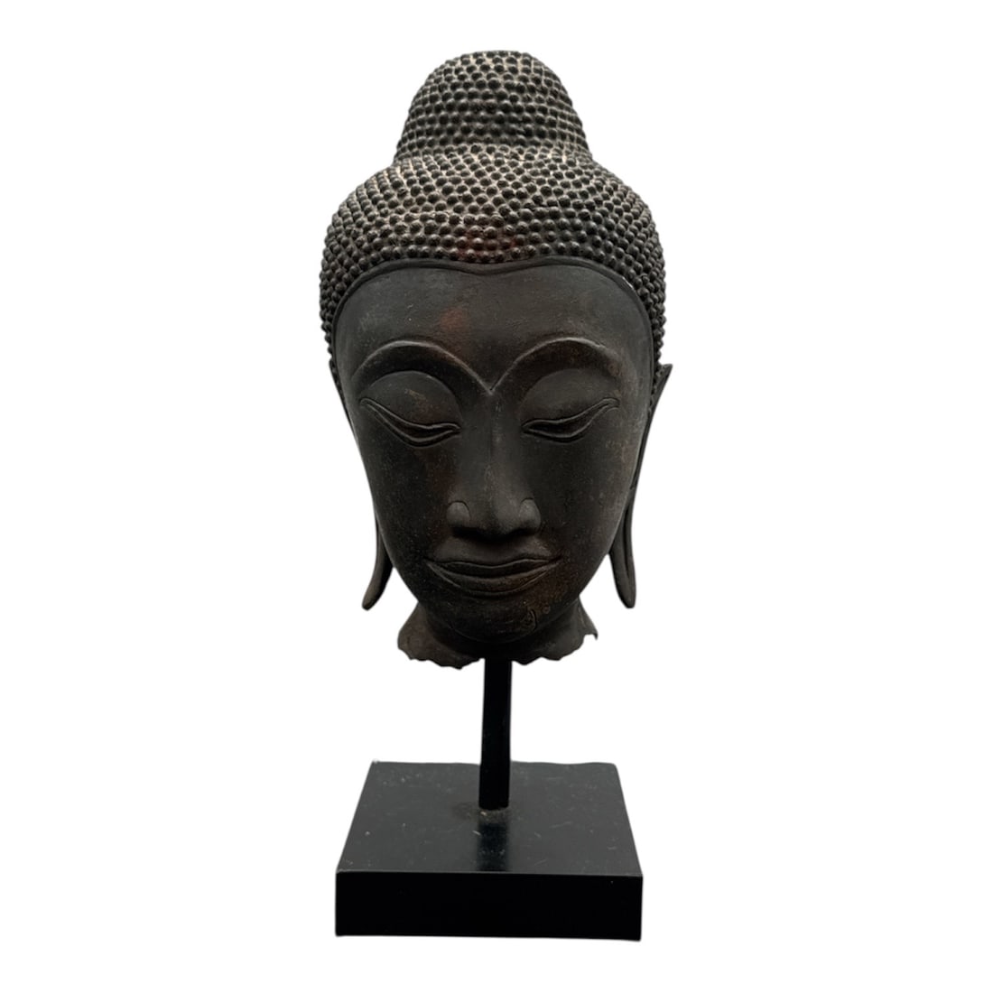 18th–19th Century Thai Bronze Buddha Head on Stand: DescriptionCast bronze head of Buddha dating to the 18th–19th century, featuring a serene expression with downcast eyes beneath gracefully arched brows. The head is modeled with tightly curled