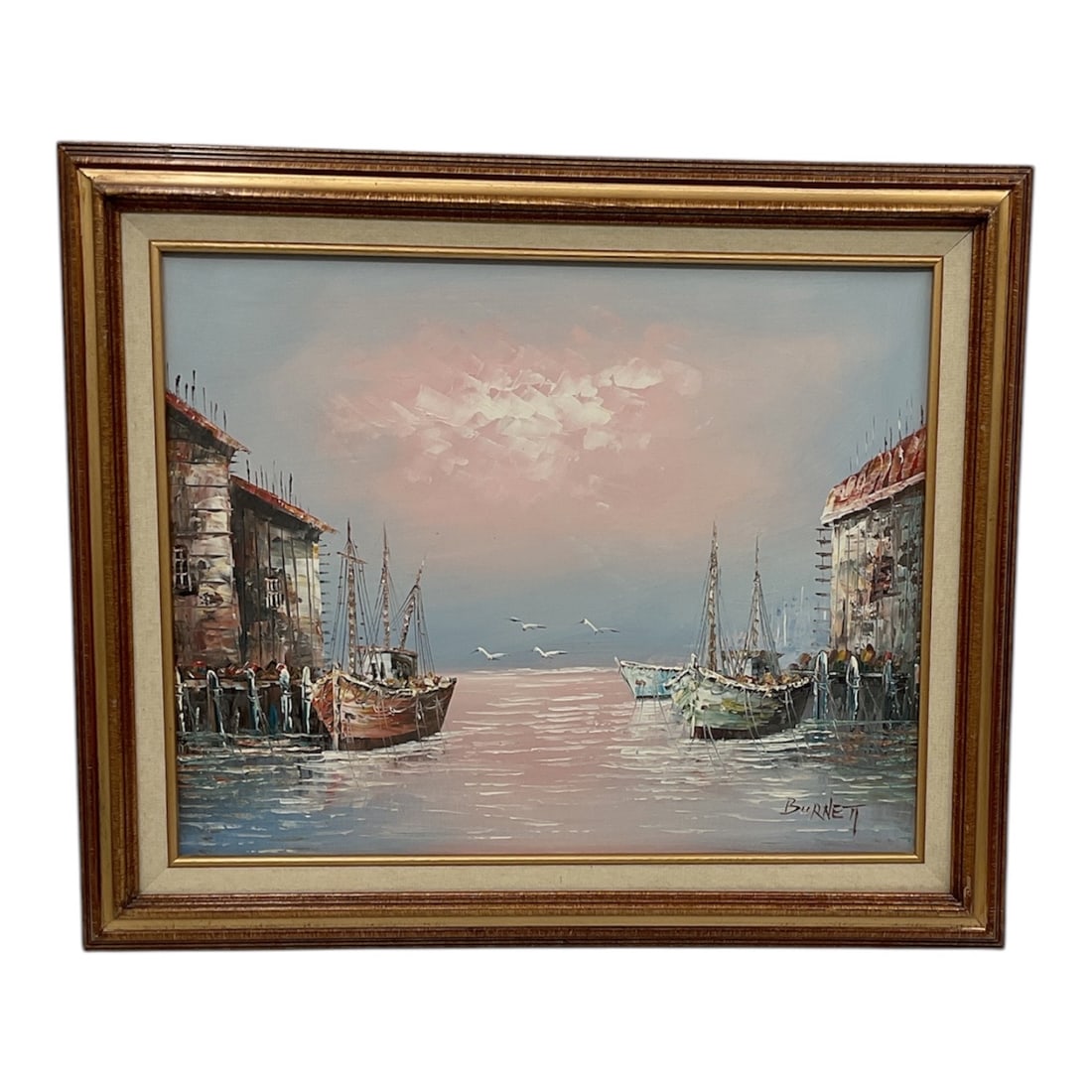 Harbor Scene by Burnett, Oil on Canvas: An atmospheric oil painting depicting a tranquil harbor scene, signed “Burnett” lower right. The composition features docked boats along a waterfront flanked by rustic buildings, opening t