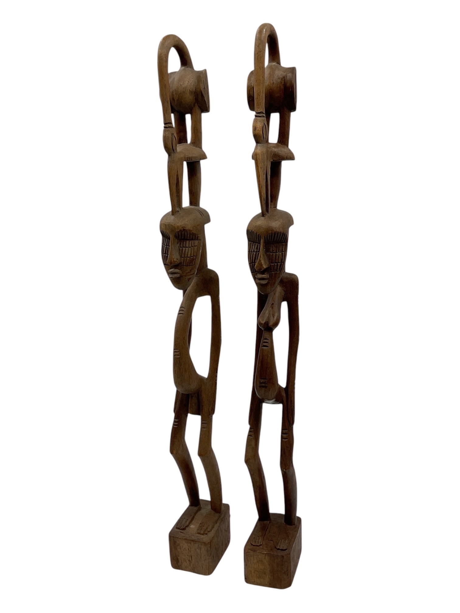 Pair of African Carved Wood Figures: Pair of hand-carved African wood figures depicting elongated standing male forms with stylized facial features and attenuated limbs. Each figure supports a circular element above the head, a design ch