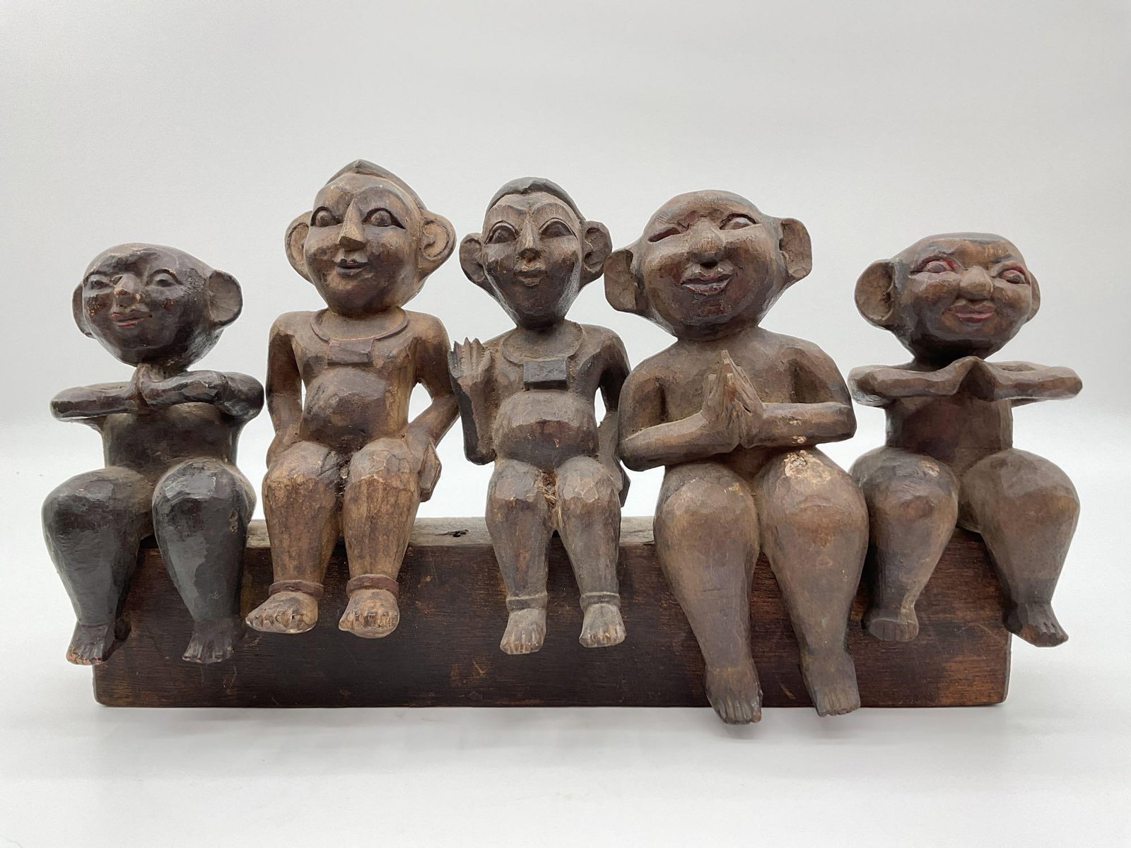 Hand-Carved Southeast Asian Folk Sculpture of Five Seated Figures: This whimsical wooden sculpture features five seated figures carved in a folk art style, each with exaggerated facial features and expressive postures. Displayed in a row on a single wooden base, the 
