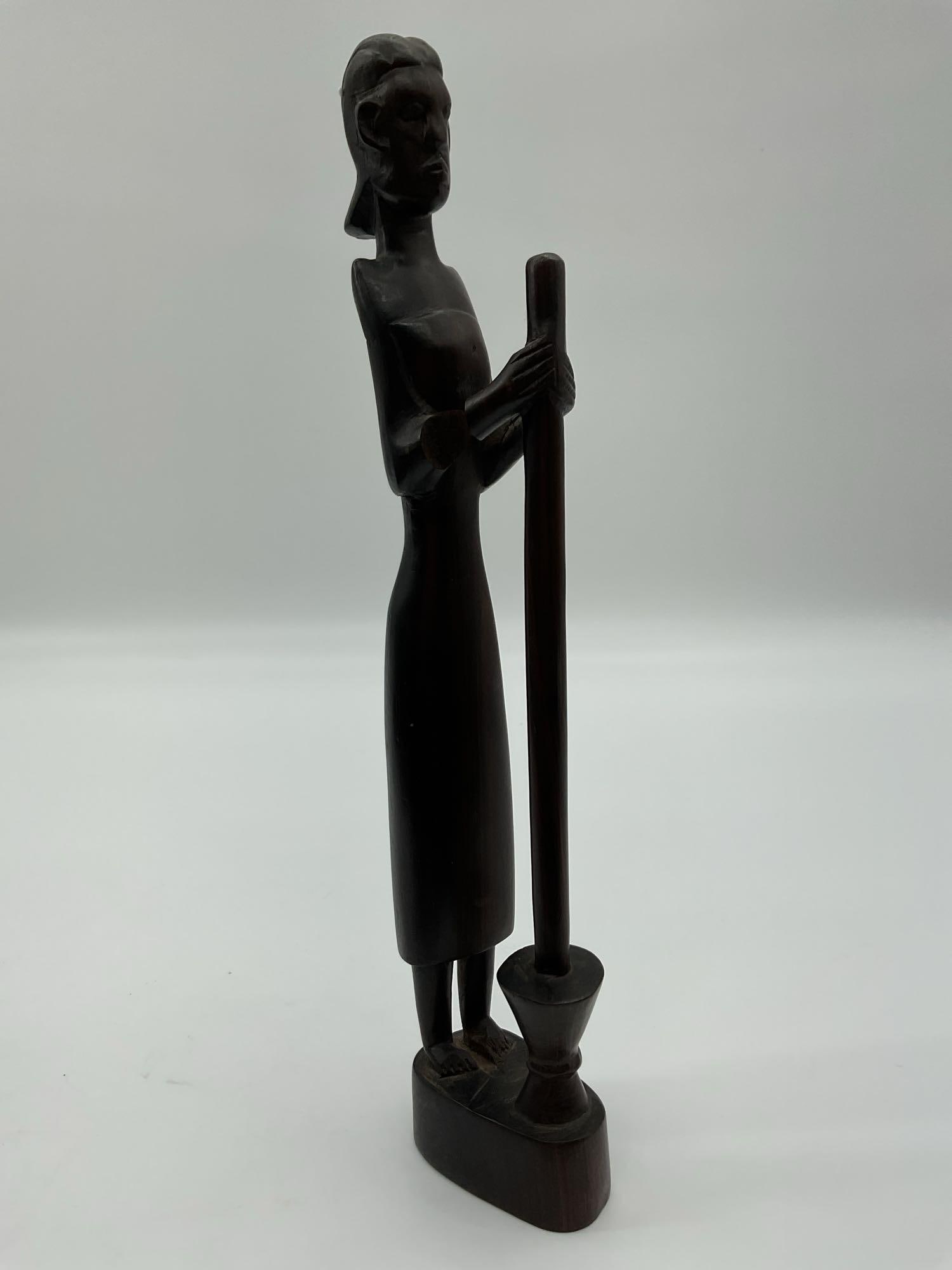 African Hand-Carved Sculpture of Woman Grinding Grain: This tall, slender wooden sculpture depicts a woman standing upright while grinding grain using a traditional mortar and pestle. Carved in a minimalist yet expressive style, the piece captures the ele
