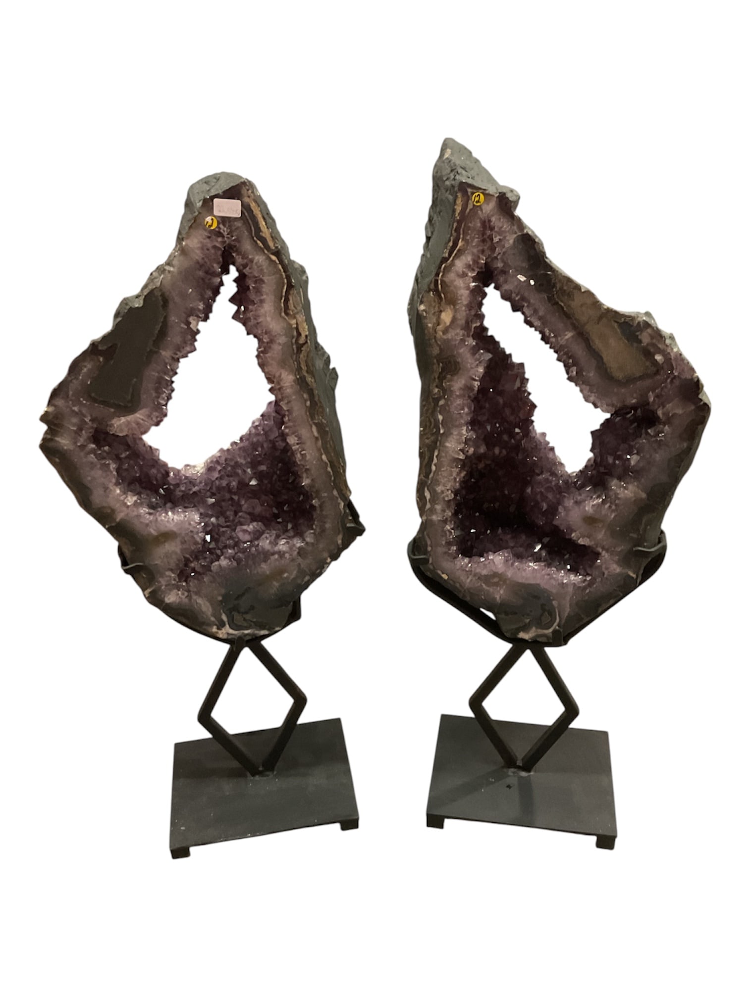 Pair of Large Amethyst Geode Rings on Metal Stands: A dramatic pair of natural amethyst geode sections, each featuring a large open central window surrounded by sparkling violet quartz crystals. The interiors range from pale lavender along the edges to