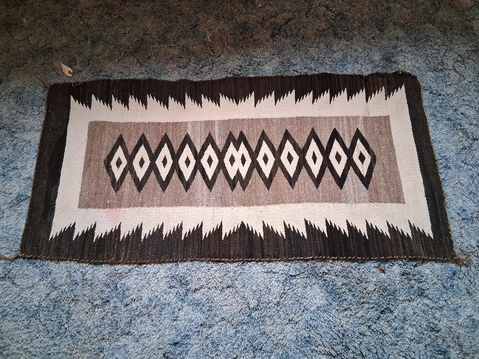 Navajo throw rug 57" long by 26" wide showing wear on one corner and slight red stain. (1 of 5)