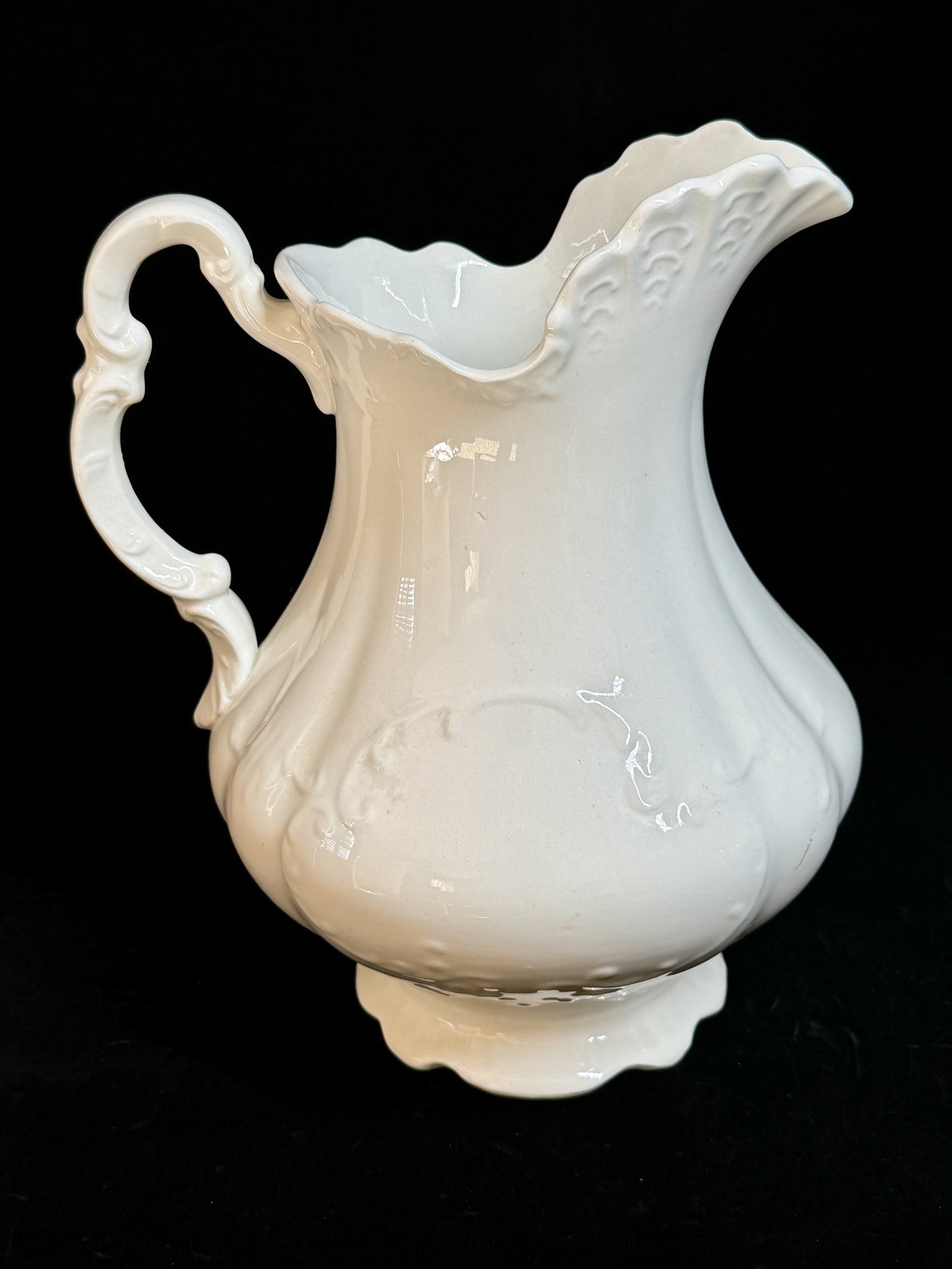 Older White Ironstone Water Pitcher with Rigory Handle: Older White Ironstone Water Pitcher with Rigory Handle DESCRIPTION: Porcelain water pitcher with a meandering pattern. All glazed white and set with an elaborate rigory handle and pie crust edging to 