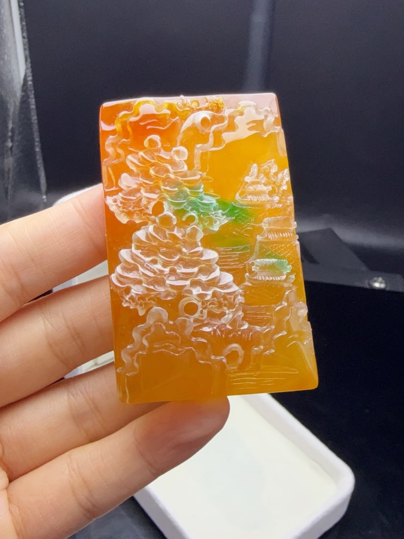 A jadeite pendant made of icy yellow jade with floating green hues, depicting a landscape. (1 of 9)