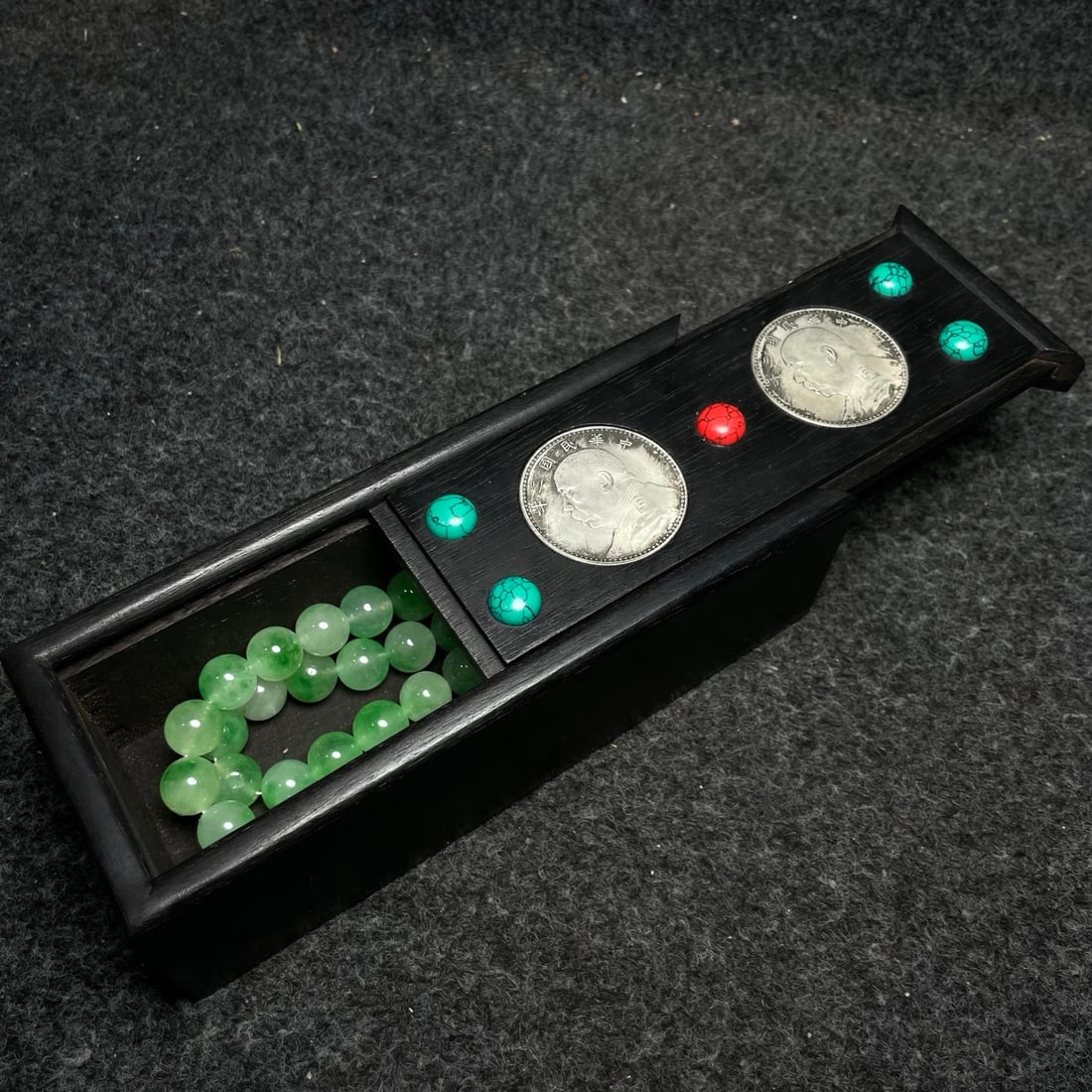 A jadeite clavicle necklace housed in an ebony wood box inlaid with silver coins.: A jadeite clavicle necklace housed in an ebony wood box inlaid with silver coins. Provenance:from the collection of George Stopher, Kent, purchased from P&M Waldo Antiques, London. Our cooperative log