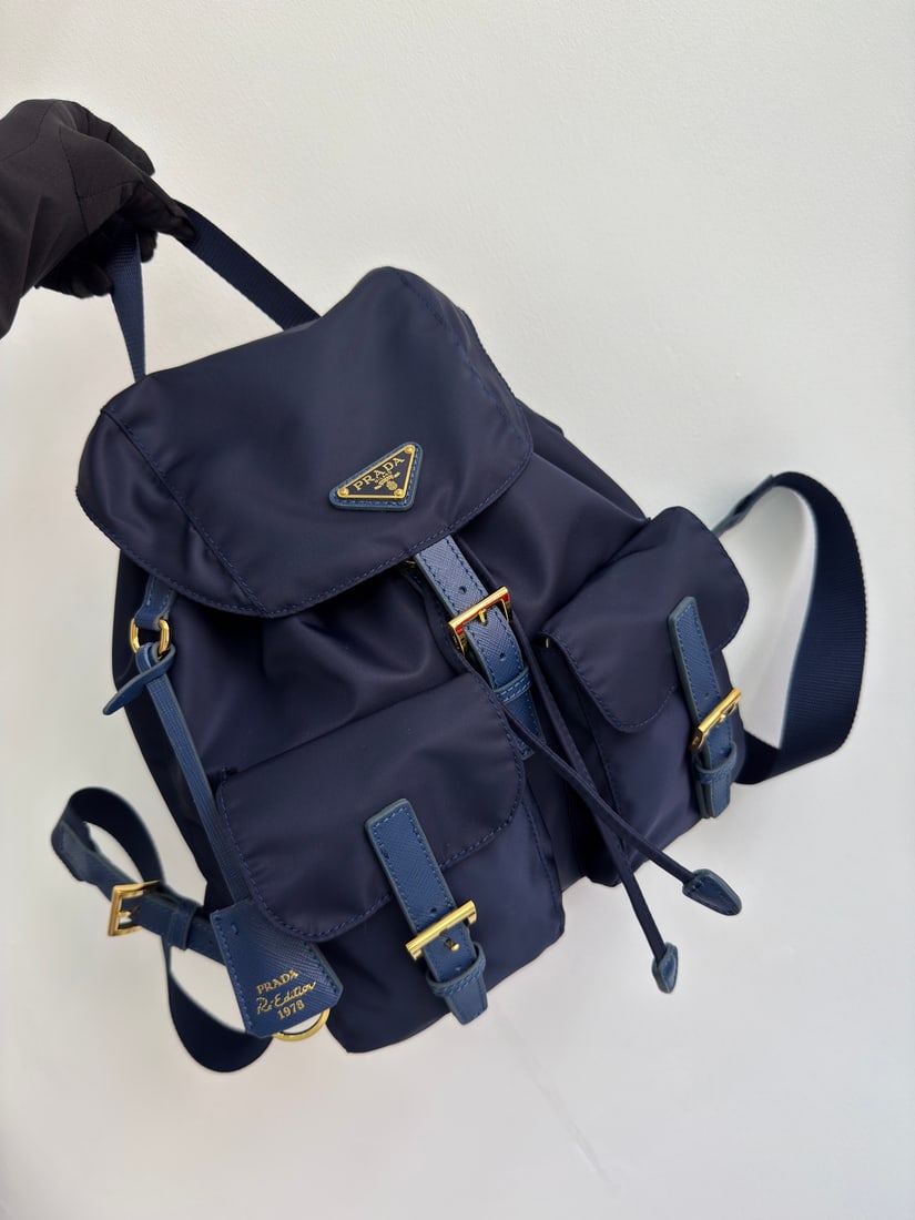 PRADA Classic Backpack with Gold Buckle: This classic backpack with gold buckles is both practical and innovative. Made with imported nylon fabric, it features adjustable shoulder straps and a woven handle, a detachable Re-Edition leather