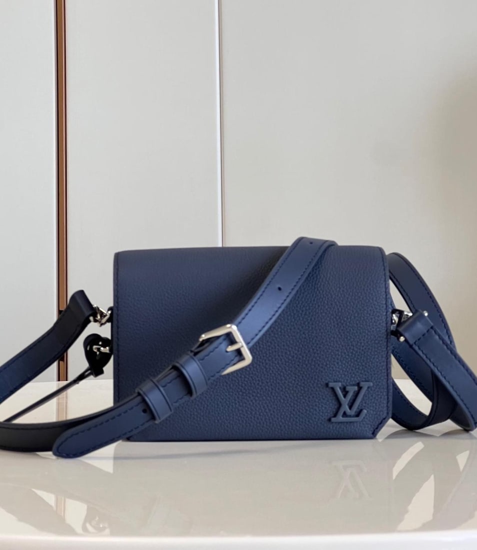 LV Fastline: The navy blue Fastline mini handbag combines grained calfskin with a distinctive Aerogram design, featuring a bias-cut flap detail and LV lettering on the front corner. A detachable shoulder strap