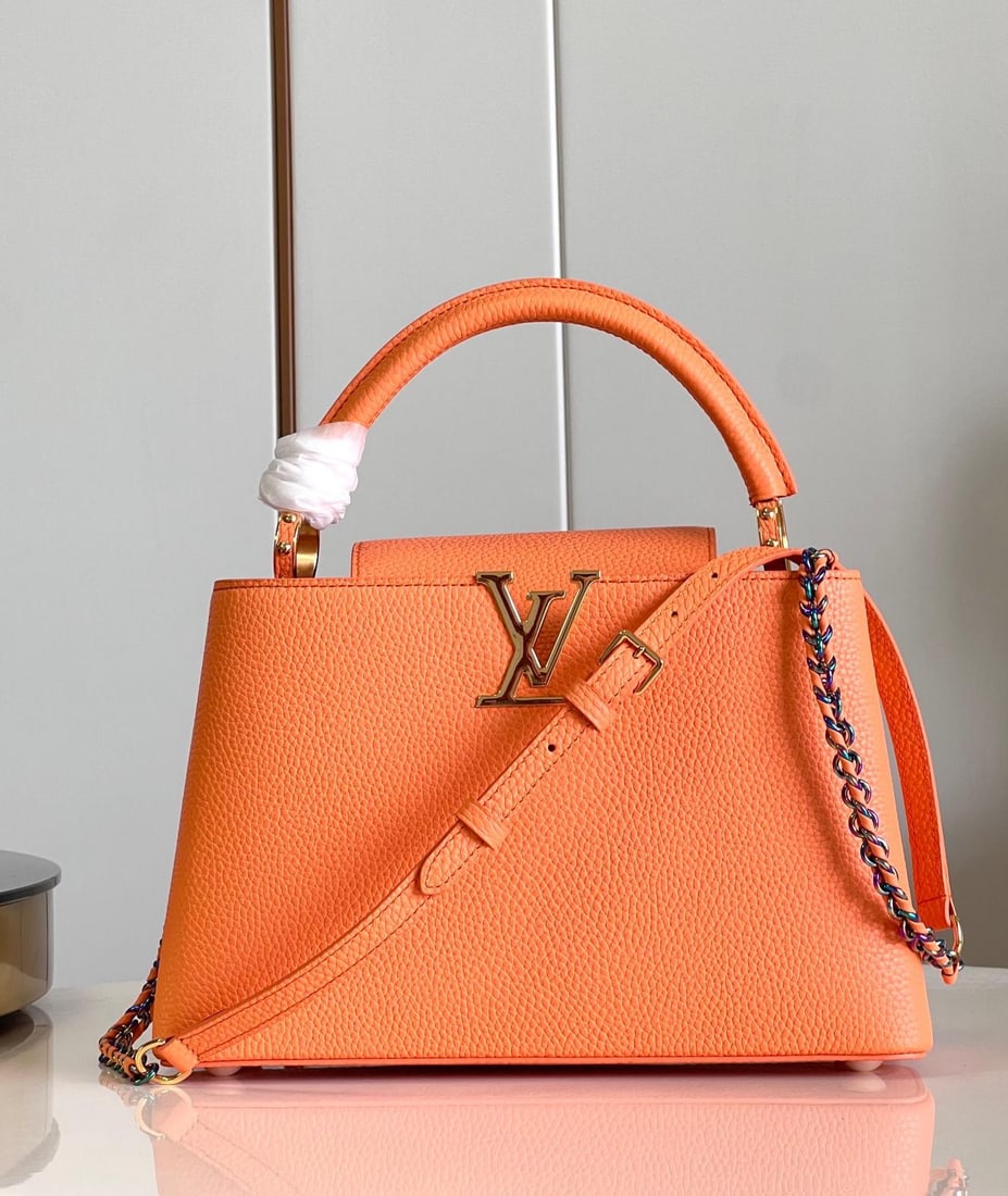 LV Capucines MM: The coral orange medium-sized Capucines MM handbag features vibrant colors on the LV logo and woven chain, contrasting with the understated elegance of the Taurillon leather body. Jewelry-like handles