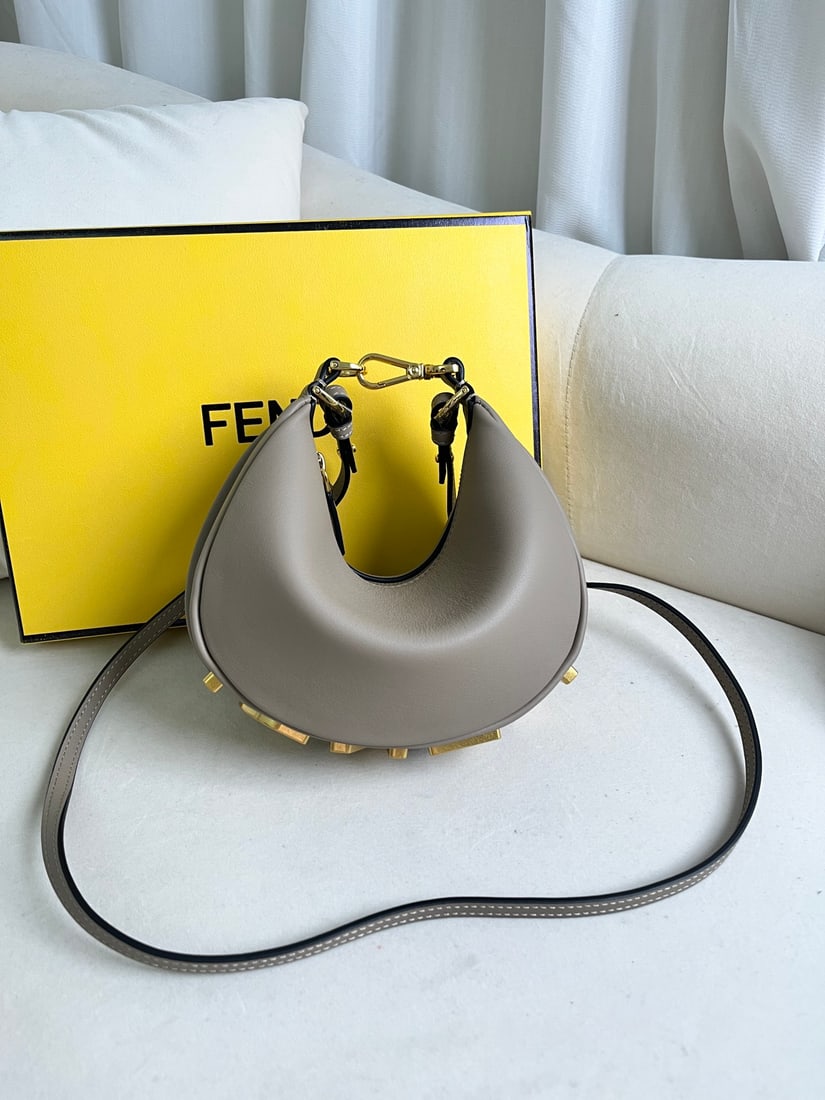 Fendi Praphy: This small grey Praphy underarm bag features a crescent shape and a classic large metal logo at the bottom. Its silhouette hugs the body's lines, creating a stylish look when worn under the arm.