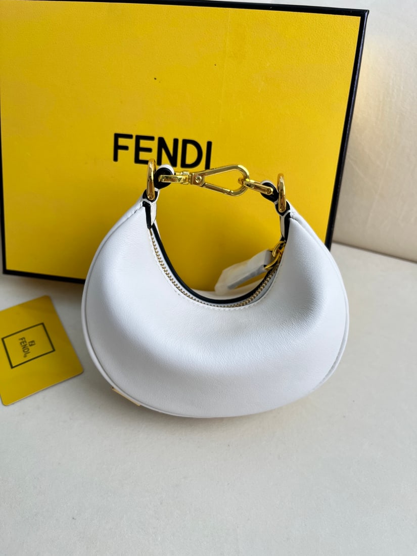 FENDI Praphy: This small white FENDI Praphy underarm bag features a crescent shape and a classic large metal logo at the bottom. The bag's silhouette hugs the body's lines, creating a stylish look when worn under
