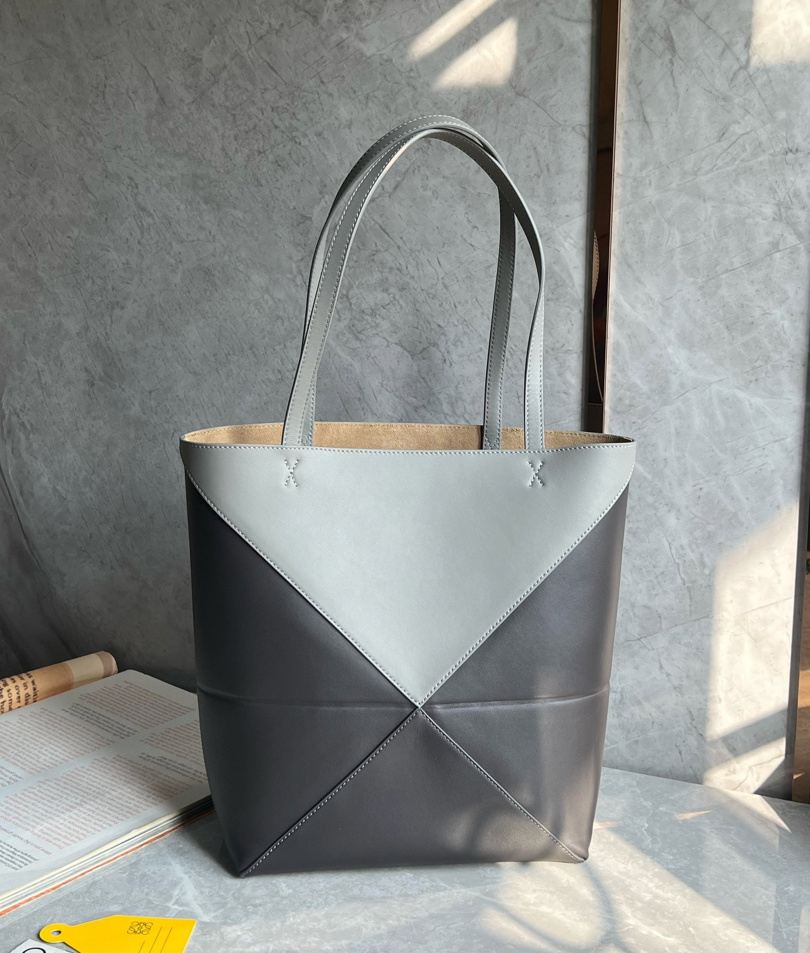 LOEWE: The LOEWE Puzzle Fold Tote bag, in a striking grey and dark grey color scheme, exudes a fashionable vibe. Made of Nappa calfskin, the Puzzle Fold Tote features clean lines inspired by origami, offerin