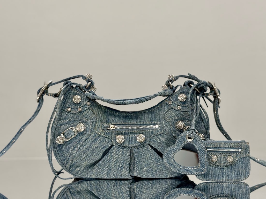 Balenciaga Le Cagole: The Balenciaga Le Cagole moon bag features denim elements and imported rhinestones. It can be worn under the arm or crossbody, and also includes a small mirror and a small pouch, demonstrating attenti