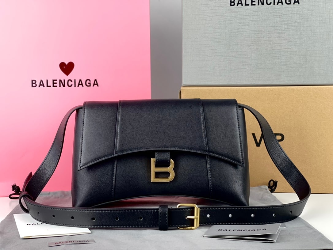 Balenciaga Hourglass: The Balenciaga Hourglass bag in black with a flat-textured finish boasts a unique and iconic curved shape that is instantly recognizable and eye-catching. Its smooth, flat surface presents a crescent 