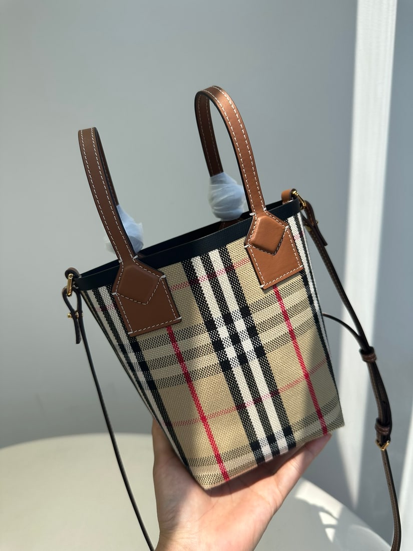 Burberry: This Burberry check London bucket tote bag is a versatile piece that can be carried by hand, over the shoulder, or crossbody. The body is crafted from a combination of check cotton canvas and top-grai