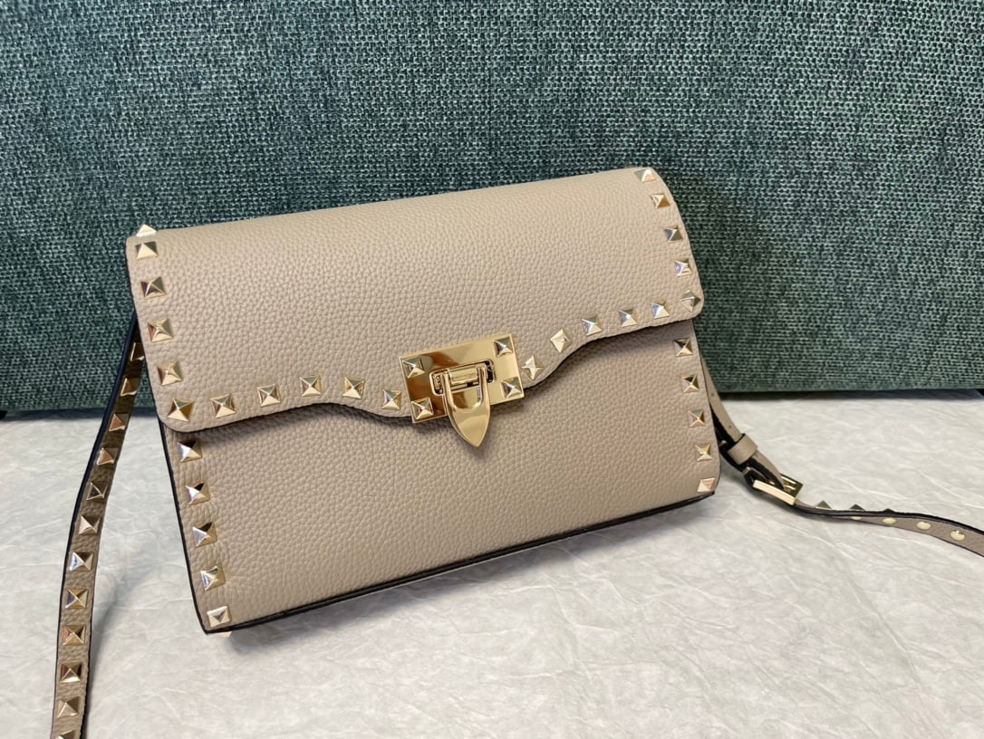 Valentino: Grey Valentino messenger bag with tumbled gold studs and a simple design. It features an adjustable shoulder strap and one interior slip pocket. Leather: Plain tumbled cowhide. Size: 22.5 x 5 x 16