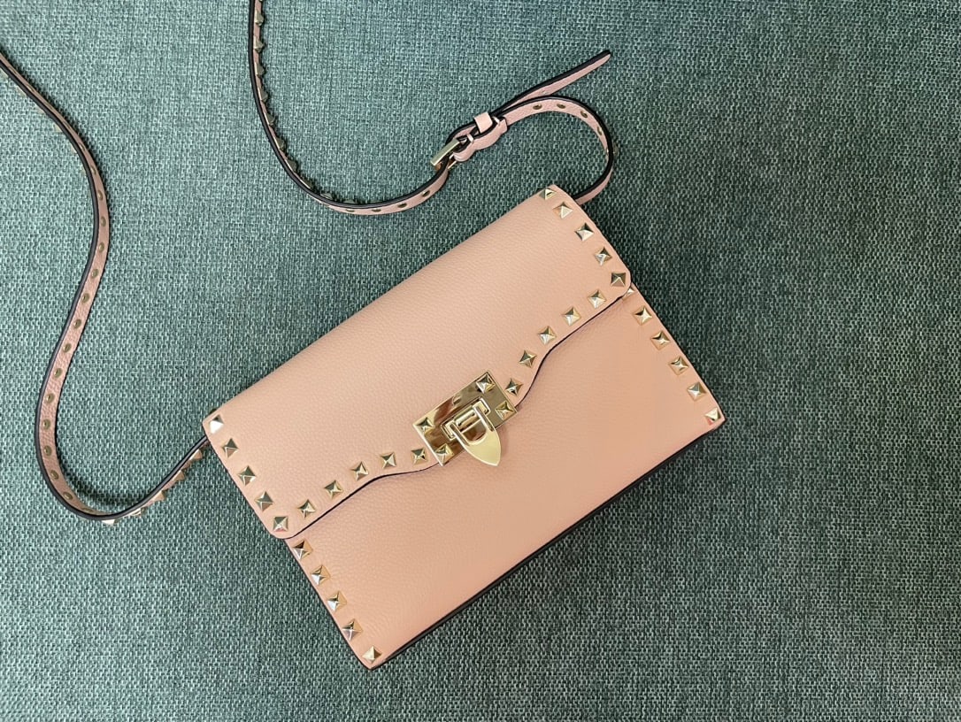 Valentino: Light pink Valentino messenger bag with tumbled gold studs and a simple design. It features an adjustable shoulder strap and one interior slip pocket. Leather: Plain tumbled cowhide. Size: 22.5 x 5 x