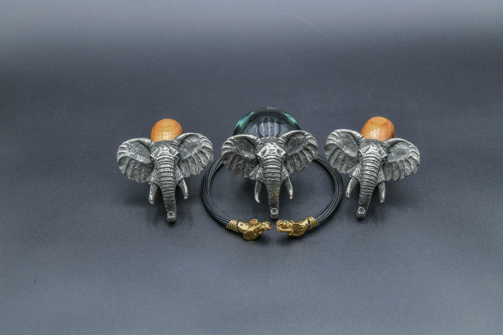 Lot of 4 Decorative Items w/Finely Sculpted Elephant Head Motifs: Lot of 4 Decorative Items w/Finely Sculpted Elephant Head Motifs. 1)Set of 2 Wood & Pewter Napkin Ring, 4"1/2L x 2"1/4H; 2)Glass Body & Pewter Elephant Paper Weight with Mark, 4"1/2L x 2"1/2H; 3)Afric