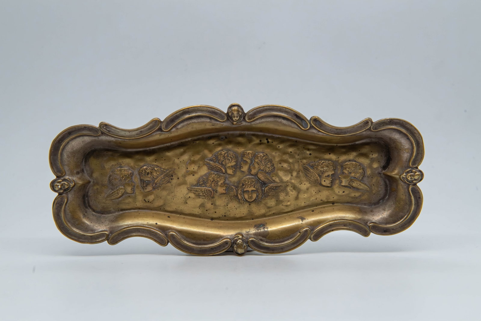 Vintage Brass Trinket Tray w/Ornate Scrolling Edges & Embossed Designs: Vintage Brass Trinket Tray w/Ornate Art Nouveau Scrolling Edges & Embossed Designs. It is embossed with a series of winged faces down the center. Measures 9"L x 3"3/4W x 1/2"H; Overall in good conditi