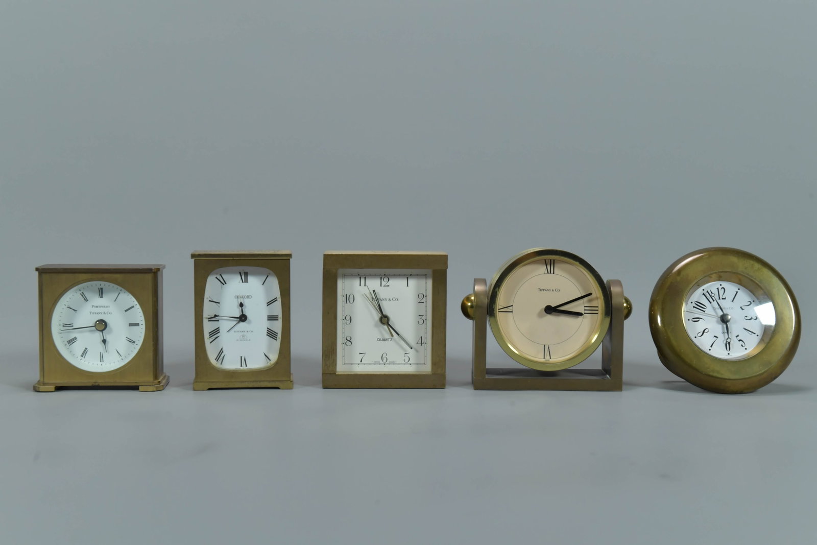 Lot of 5 Vintage Tiffany & Co. Brass Desk Clocks: Lot of 5 Vintage Tiffany & Co. Brass Desk Clocks. 1) Small round brass clock & "Quartz" printed on the dial, Diameter 4", Swiss; 2) Portfolio Tiffany & Co. quartz brass clock, 3"H x 3"w x 1"1/2D, Germ