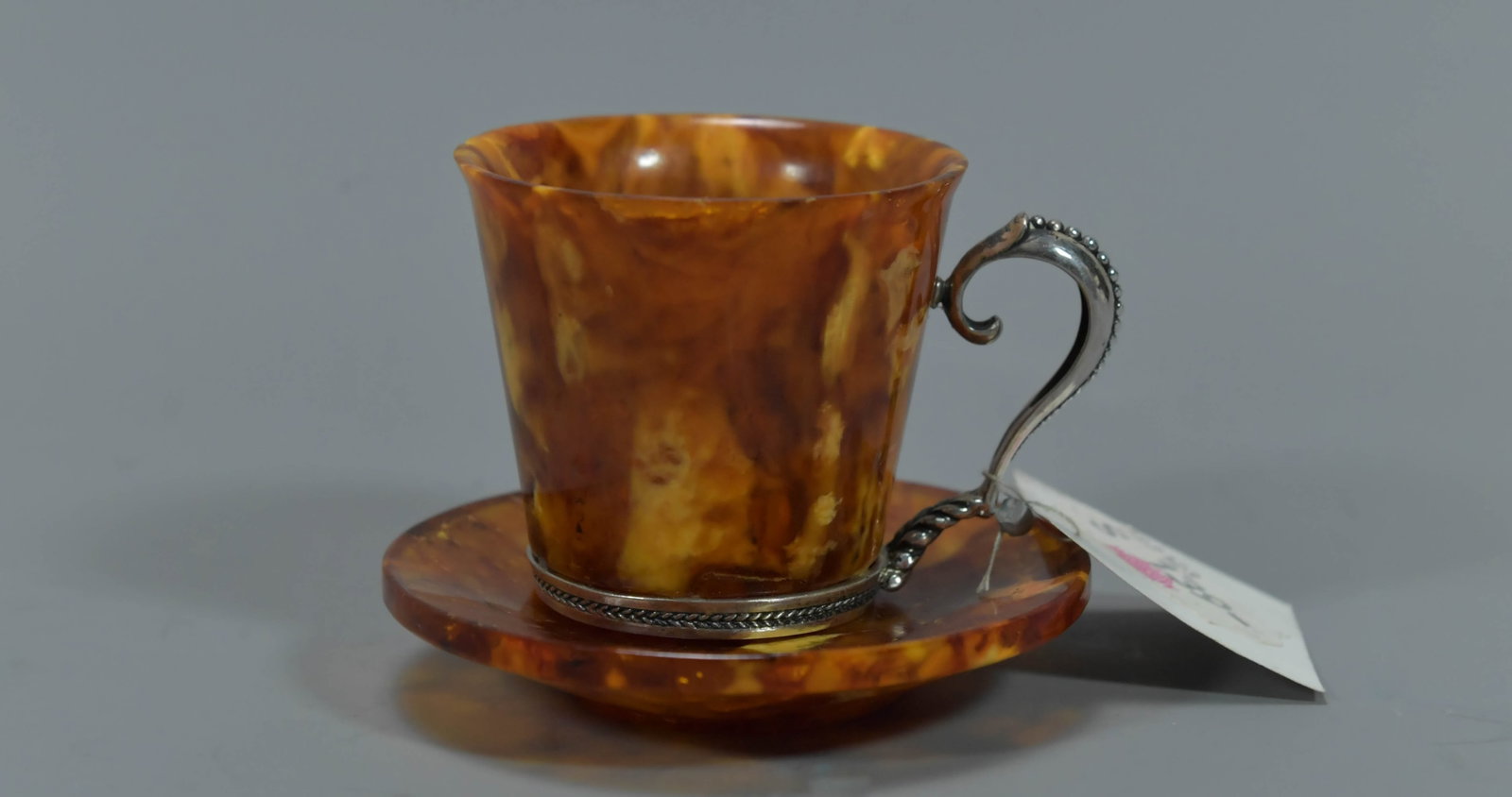 Beautiful Vintage Russian Amber Teacup & Saucer Set w/Ornamental Silver Handle & Rim: Beautiful Vintage Russian Amber Teacup & Saucer Set w/Ornamental Silver Handle & Rim. Amber teacup 2"1/4W x 2"H, Total weight 50.2gm; Amber saucer 2"1/4W, weight 31.9gm; In good condition, (Stand Not 