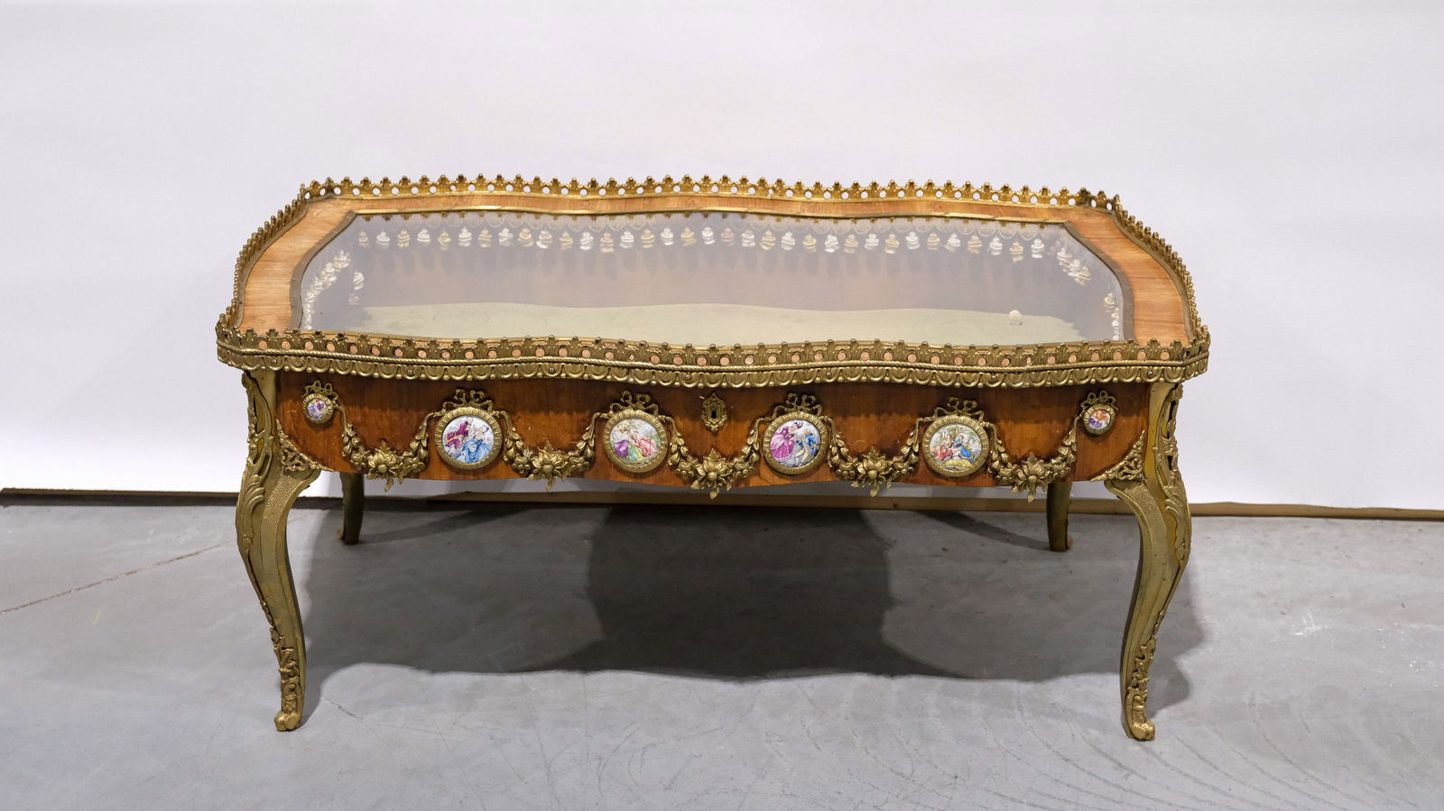 A 20th Century rectangular shaped Louis XV style display coffee table with gilt brass mounts: A 20th Century rectangular shaped Louis XV style display coffee table with gilt brass mounts and small porcelain plaques. W: 107,5 cm - H: 48,5 cm - D: 65 cm