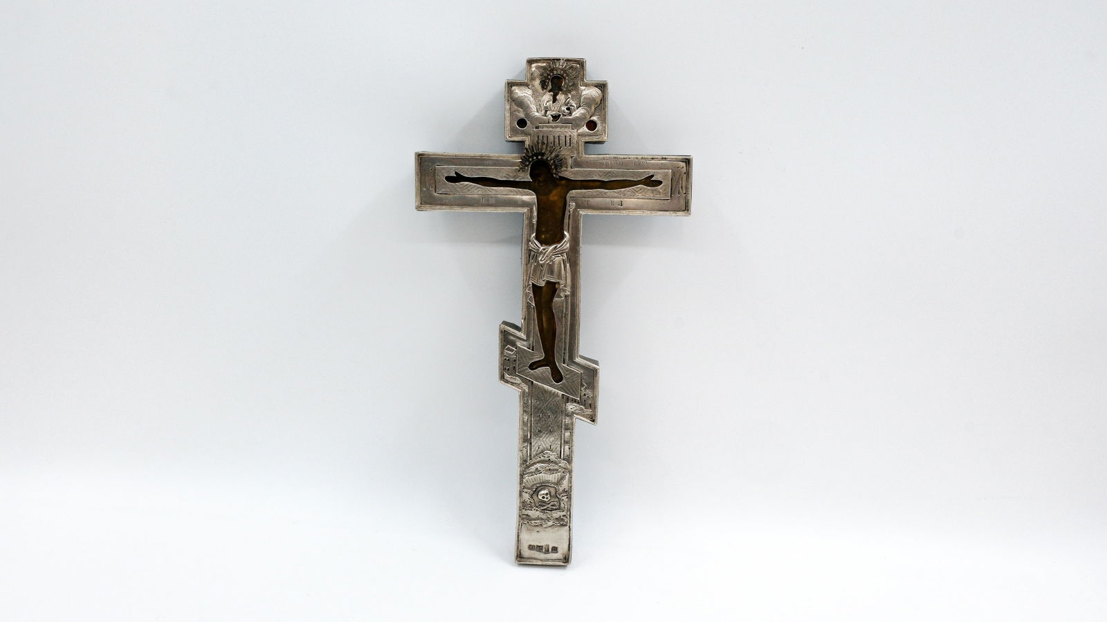 An antique Russian tempera on wood crucifix with silver oklad and engraved details: An antique Russian tempera on wood crucifix depicting the crucified Christ with God the Father above and Golgotha below, overlaid with a finely engraved and repoussé silver oklad, marked with silver
