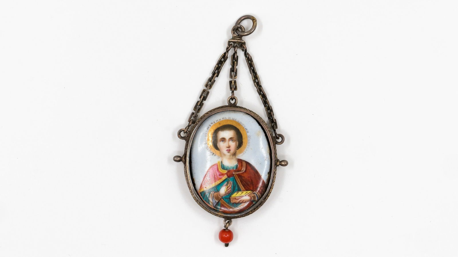 An antique Russian silver and enamel pendant of Saint Panteleimon: An antique Russian silver and enamel pendant of Saint Panteleimon holding a medicine box, mounted in an oval silver frame with chain suspension and coral bead finial. 19th century. H: 5,1 - W: 4,3 c