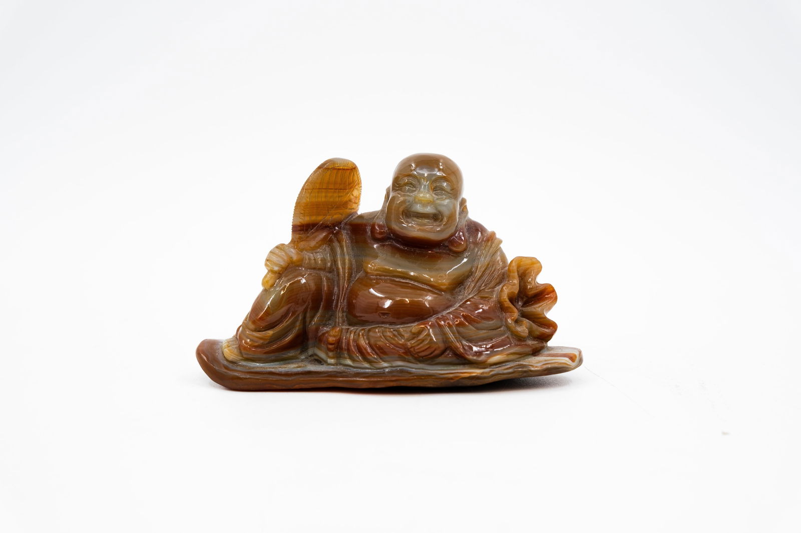 A Chinese carved brown jade sculpture of a laughing Buddha with fan: A Chinese carved brown jade sculpture of a laughing Buddha holding a fan.  19th/20th century.  Condition: the fan has been restored. A condition report is available on request.  H: 8 - 14 cm
