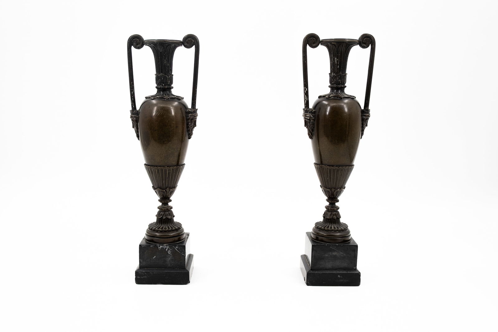 An antique pair of patinated bronze vases with handles and crowned male heads: An antique pair of patinated bronze vases with handles and crowned male heads. Footed on black marble bases. 19th century. H: 34 cm