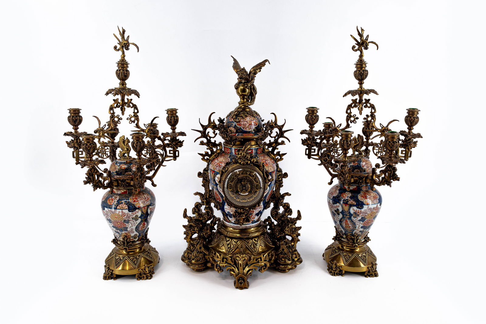 A large antique Japanese Imari-decorated porcelain mantel clock set: A large antique Japanese Imari decorated porcelain mantel clock with parcel-bronze mounts with two matching candelabras marked by H.Luppens & Cie, Bruxelles. Late 19th century. Condition: the th