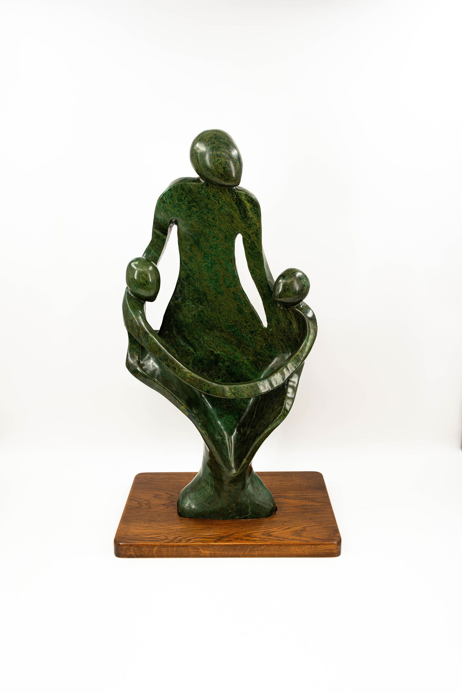 A large and abstract African Tribal art carved stone sculpture figural group: A large and abstract African Tribal art sculpture figural group in carved and polished serpentine style stone representing a figure with two children. Mounted on a wooden base. Signed, circa 1960-19