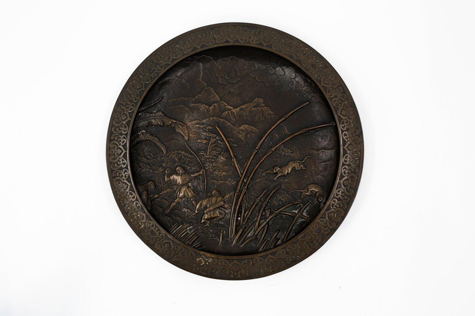 An antique Japanese patinated bronze relief decorated wall plate: An antique Japanese patinated bronze relief wall plate decorated with a hunting scene. Meiji, late 19th century. W: 37,5 cm