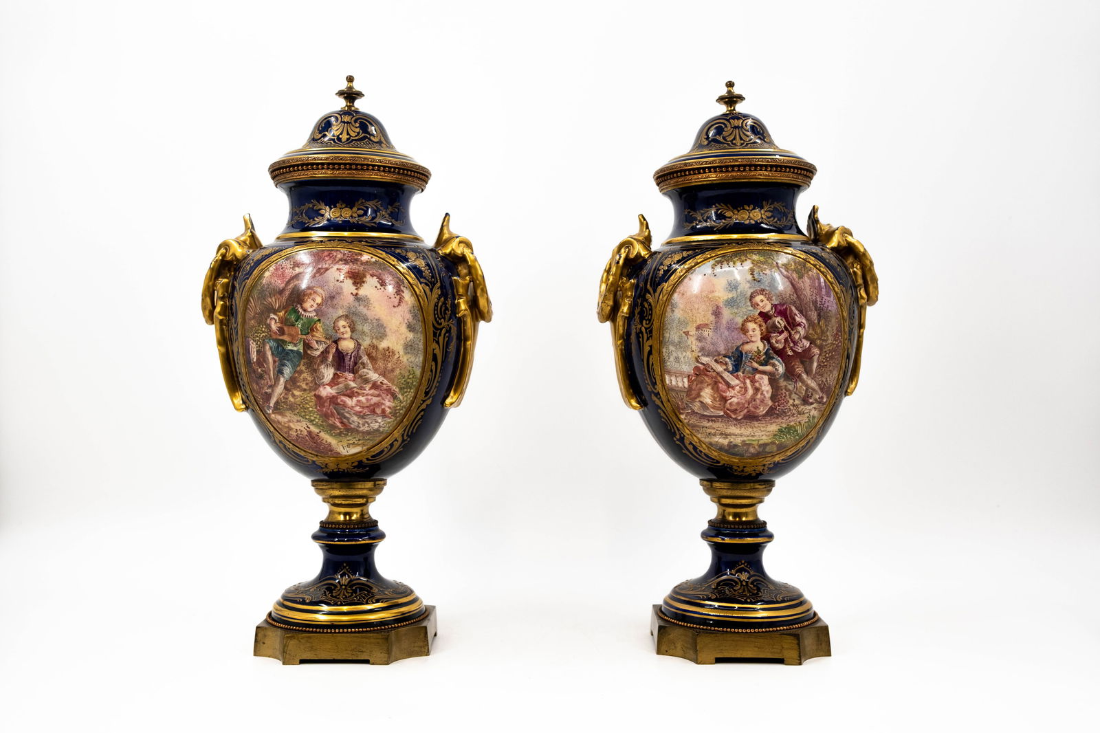 An antique pair of French Sevres style decorated gilt and cobalt covered ceramic vases: An antique pair of French Sevres style decorated gilt and cobalt covered ceramic vases with brass mounting. Decorated with hand painted romance scenes. Marked, circa 1900. H: 44,5 cm