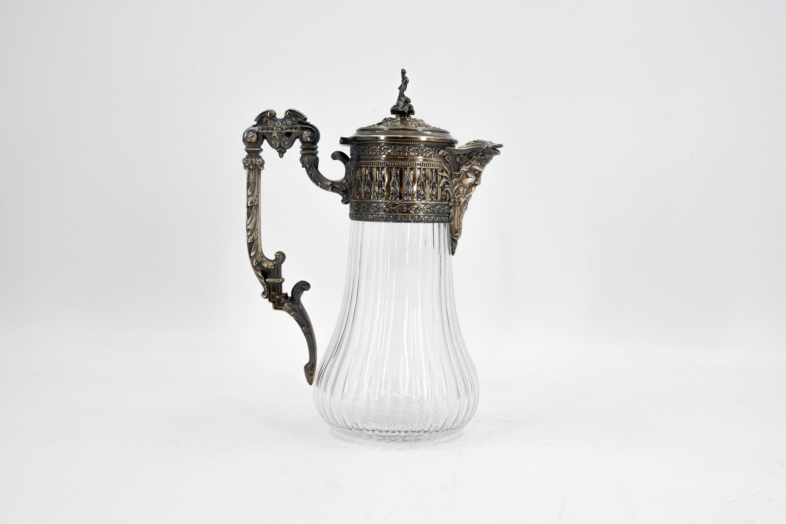 An antique crystal serving pitcher with richly decorated silver mounting: An antique crystal serving pitcher with richly decorated silver mounting and Bacchus shaped head. Hallmarks and late 19th century. H: 27,5 cm