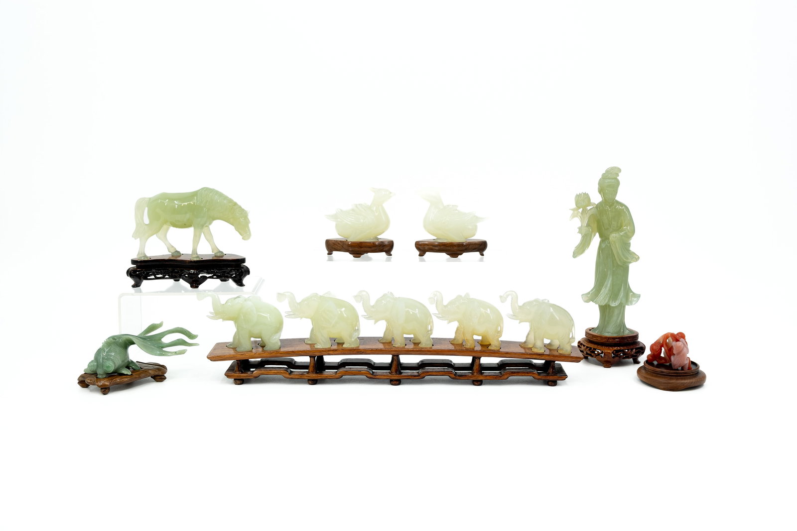 A composed collection of 11 variously shaped figural Chinese carved jade sculptures: A composed collection of 11 variously shaped Chinese green, red and white carved jade sculptures. All are footed on a wooden base. 19th/20th century. H: 3,3 - 17 cm, smallest to largest without base