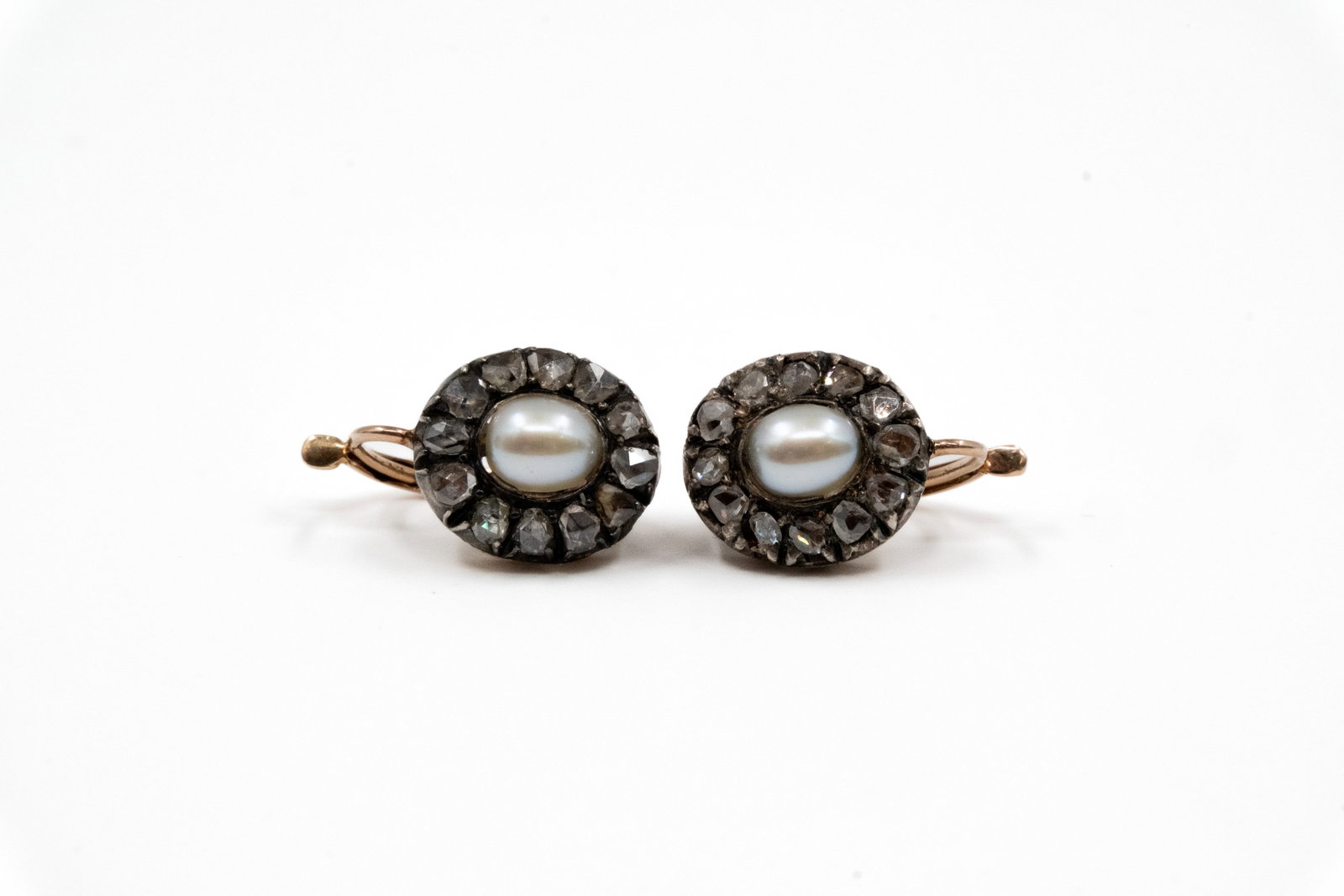 A pair of 18k gold and silver earrings set with a pearl and rose-cut diamonds: A pair of 18k gold and silver earrings set with a pearl and rose-cut diamonds. Each oval earring centred with a pearl, within a border of rose-cut diamonds, with gold hook fittings. Total weight: 5,5g